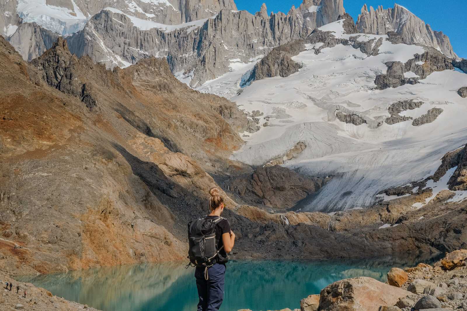 A hiker at a glacial tarn below jagged peaks