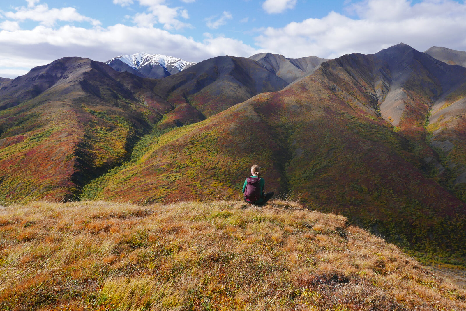 A figure rests on a tundra knoll above an autumn valley
